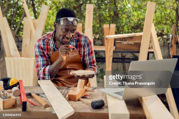 male carpenter in plaid shirt testing wood plank evenness at workshop in front of laptop - customized stock-fotos und bilder