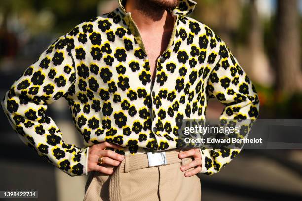 Alejandro Acero wears a white with black and yellow flower print pattern high neck zipper sweater, high waist beige long shorts, a beige matching...