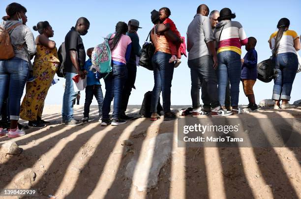 Immigrants from Haiti, who crossed through a gap in the U.S.-Mexico border barrier, wait in line to be processed by the U.S. Border Patrol on May 20,...