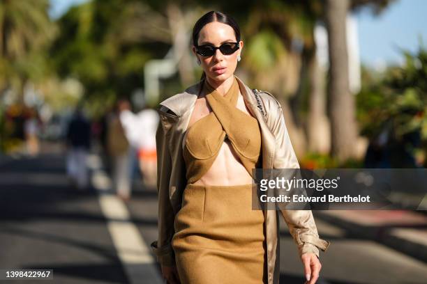 Sira Pevida wears black sunglasses, a beige long trench coat, a brown halter-neck / cropped / strappy top, a matching brown high waist tube midi...