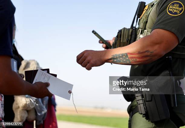 Border Patrol agent, who has an American flag tattoo honoring his father, checks the documents of immigrants who crossed through a gap in the...