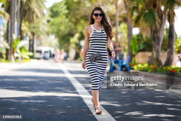 Eva Colas wears black sunglasses from Dior, silver and diamonds earrings, a navy blue and white striped print pattern halter-neck / tank-top / midi...