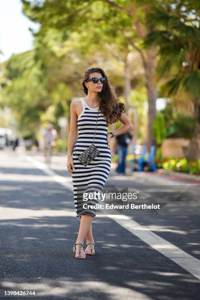 Eva Colas wears black sunglasses from Dior, silver and diamonds earrings, a navy blue and white striped print pattern halter-neck / tank-top / midi...