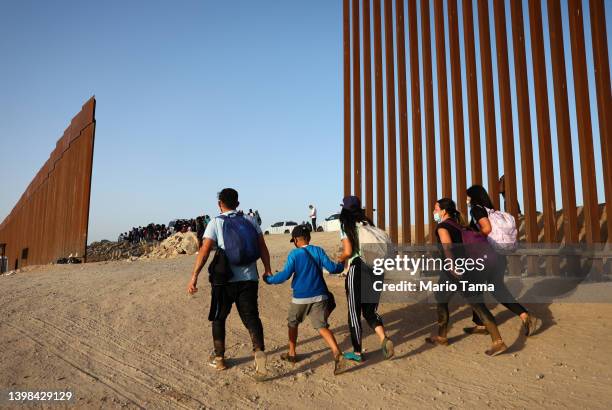 Immigrants cross through a gap in the U.S.-Mexico border barrier as others await processing by the U.S. Border Patrol on May 20, 2022 in Yuma,...