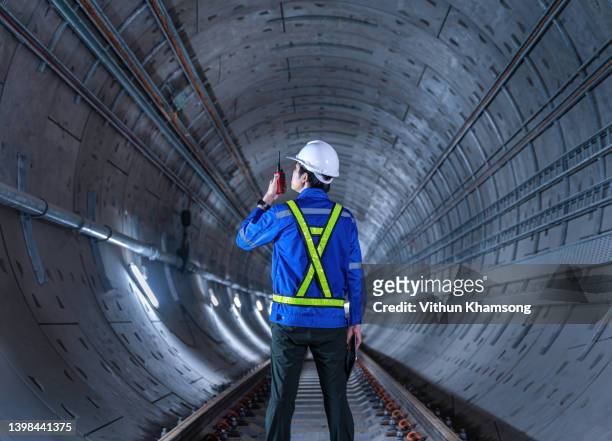 tunnel engineering and white safety helmet working and using digital tablet in dark railway tunnel construction site area with copy space. engineer checking underground railway tunnel - railroad track stock-fotos und bilder