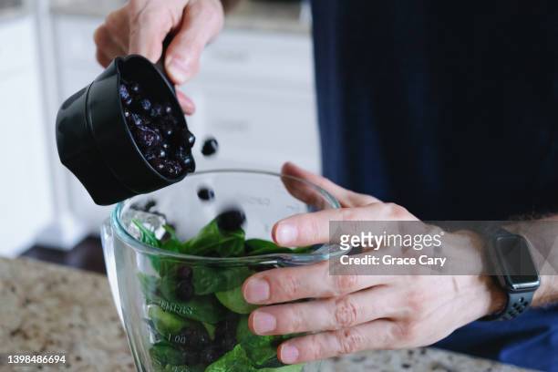 man pours blueberries into blender jar with spinach - berries and hand stock-fotos und bilder