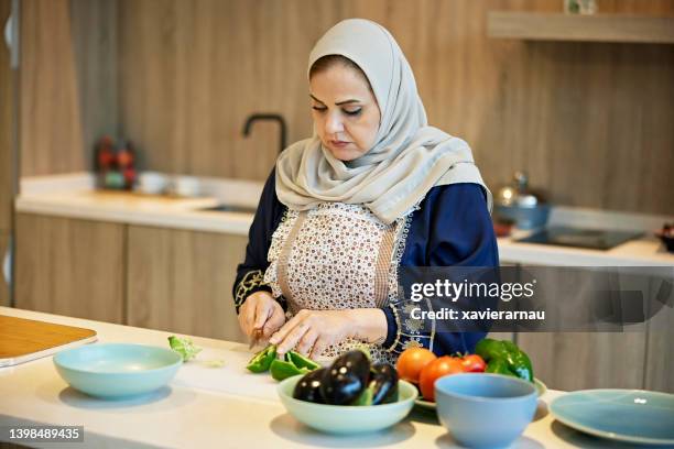 mature saudi woman chopping vegetables in kitchen - women with hijab stock pictures, royalty-free photos & images