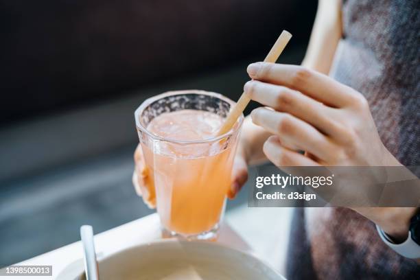 close up shot of young woman drinking a glass of fresh iced pink lemonade with eco-friendly straws during meal in cafe. sustainable lifestyle, eco trend, going green lifestyle - straw stock-fotos und bilder