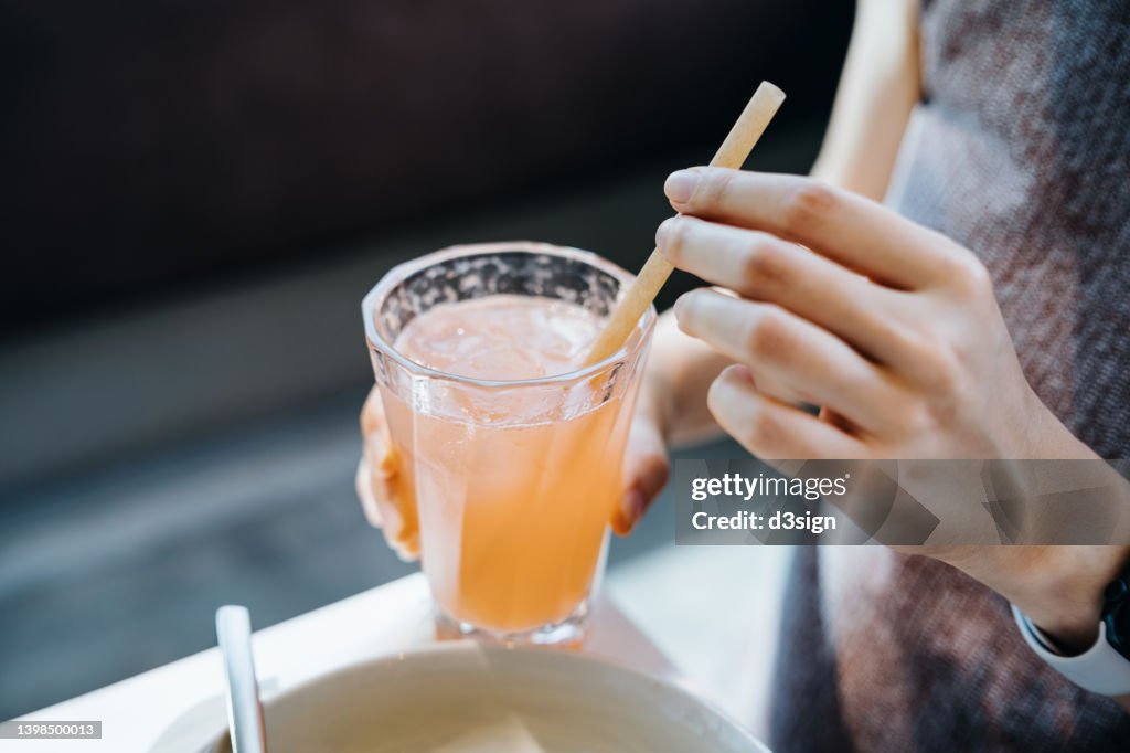 Close up shot of young woman drinking a glass of fresh iced pink lemonade with eco-friendly straws during meal in cafe. Sustainable lifestyle, eco trend, going green lifestyle