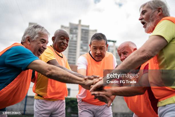 senior men with stacked hands before a match on the soccer field - sports management stock pictures, royalty-free photos & images