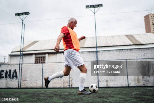 senior man kicking a ball on the soccer field - senior kicking stock pictures, royalty-free photos & images