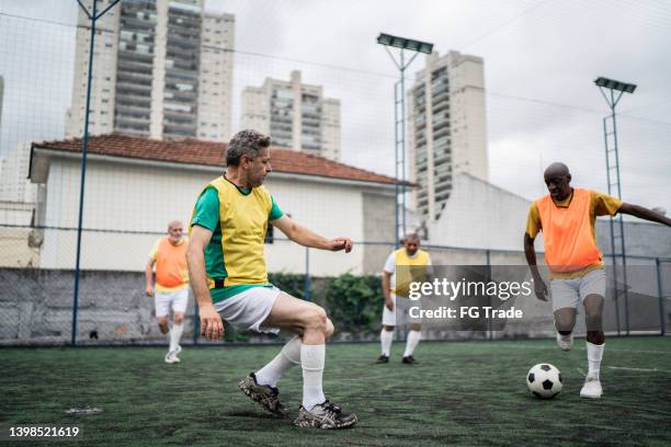 reife männer, die auf dem fußballplatz spielen - amateur stock-fotos und bilder