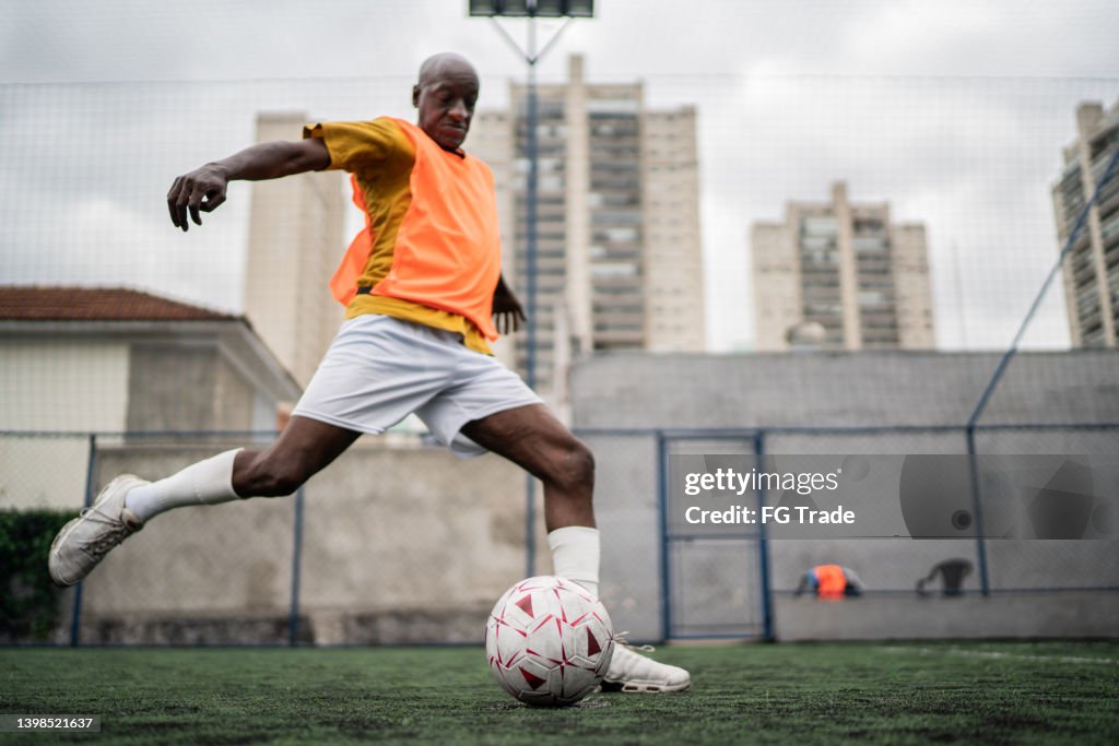 Hombre maduro pateando la pelota de fútbol en el campo de fútbol