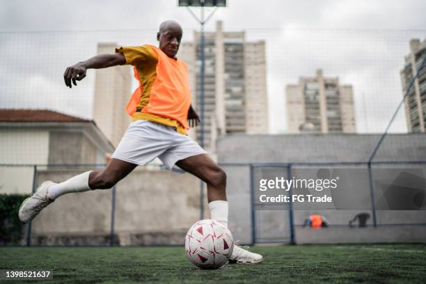 mature man kicking the soccer ball on the soccer field - schoppen lichaamsbeweging stockfoto's en -beelden