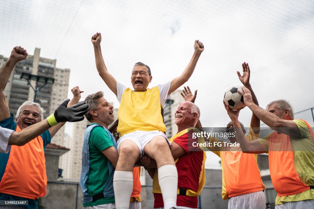 Männer, die einen von ihnen tragen und auf dem Fußballplatz den Gewinn eines Spiels feiern