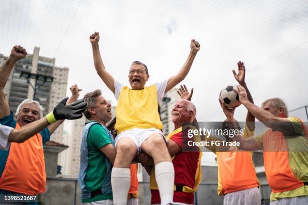 männer, die einen von ihnen tragen und auf dem fußballplatz den gewinn eines spiels feiern - amateur stock-fotos und bilder