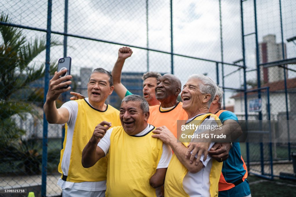 Senior men taking selfies or filming using mobile phone on the soccer field