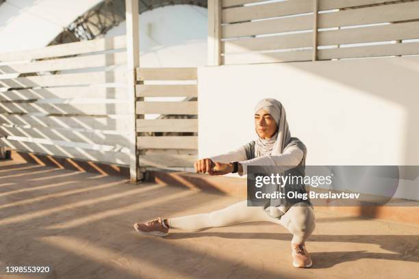 islamic woman in hijab exercising outdoors in morning, warming up and stretching legs - arabische muster stockfoto's en -beelden