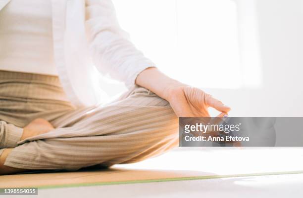 anonymous woman is meditating sitting in lotus position on a yoga mat. close-up of yoga mudra with hand. concept of relaxation exercises - 胡坐　横 ストックフォトと画像
