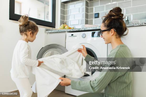 mother and child girl little helper loading washing machine. - home cleaning stock-fotos und bilder