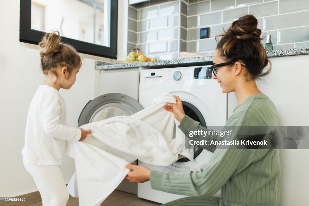 Mother and child girl little helper loading washing machine.