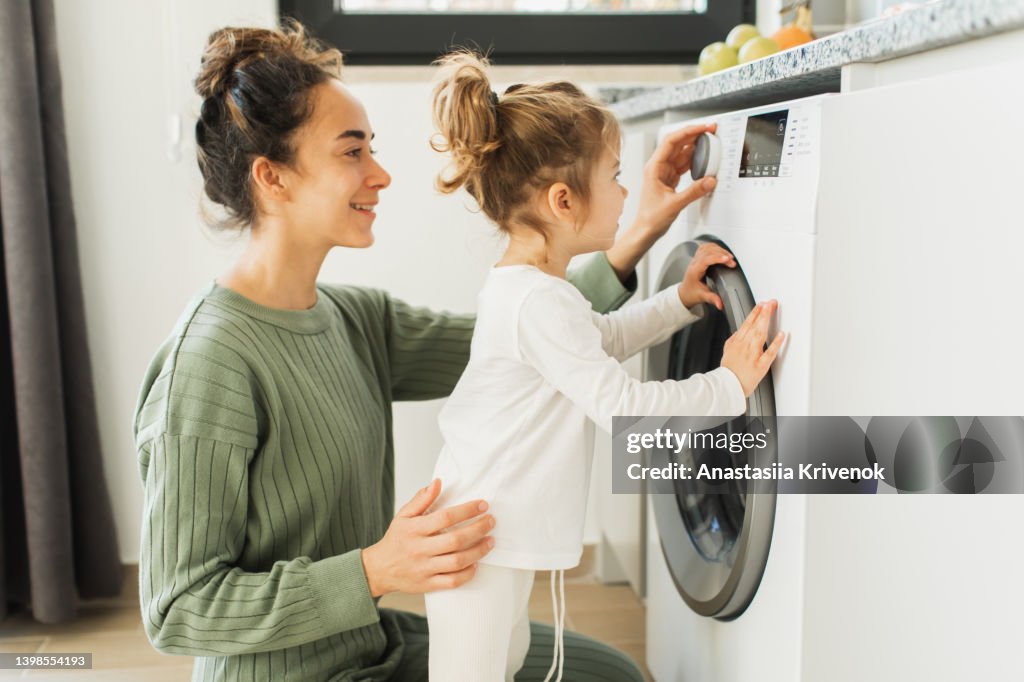 Mother and child girl little helper loading washing machine.