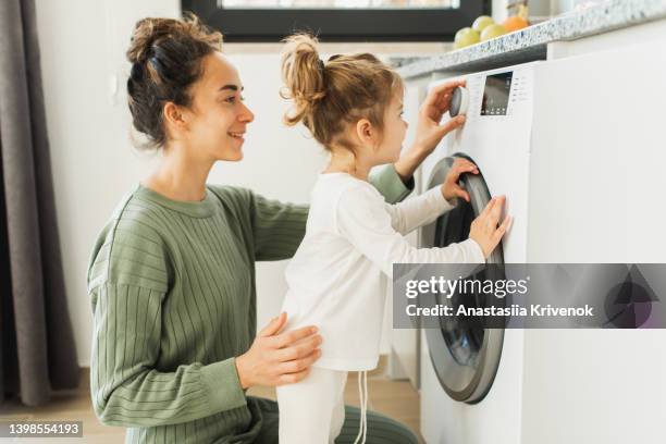 mother and child girl little helper loading washing machine. - wasserette stockfoto's en -beelden