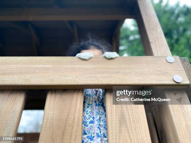 mixed-race young girl enjoys playing peekaboo outdoors in tree house playset - playhouse stockfoto's en -beelden