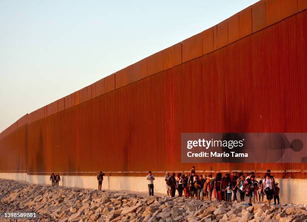 Immigrants walk along the U.S.-Mexico border barrier on their way to await processing by the U.S. Border Patrol after crossing from Mexico on May 21,...