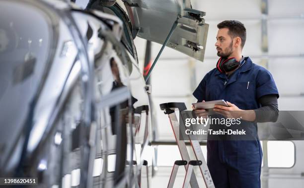männlicher aero-ingenieur mit klemmbrett-überprüfung am hubschrauber im hangar - helicopter rotors stock-fotos und bilder