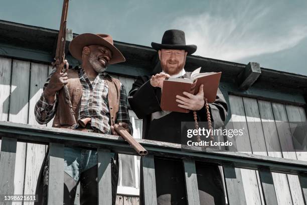 handsome redhead priest and a black cowboy in an authentic wild west setting - handsome cowboy stock pictures, royalty-free photos & images