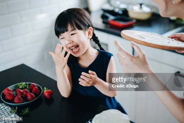 happy young asian mother and daughter having fun baking together in the kitchen. mother putting fresh cream on nose of her daughter while decorating a cake at home. family baking at home together. diy. birthday and celebration concept - passion fruit photos et images de collection