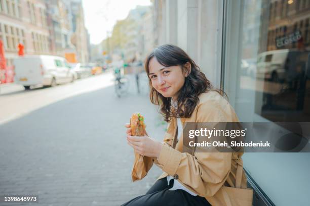 mujer sentada y comiendo panini fuera de la tienda - panini fotografías e imágenes de stock