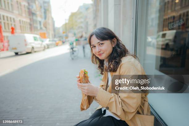 woman sitting and eating panini outside the shop - sandwich stockfoto's en -beelden