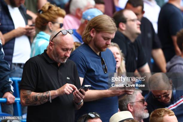 Fans check their mobile phones during the Premier League match between Chelsea and Watford at Stamford Bridge on May 22, 2022 in London, England.