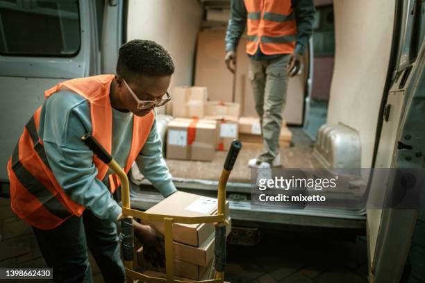 young female delivery worker loading packages on a hand truck - night delivery stock pictures, royalty-free photos & images