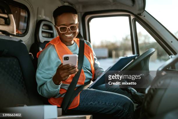 young smiling female delivery driver texting while working - bestelwagen stockfoto's en -beelden