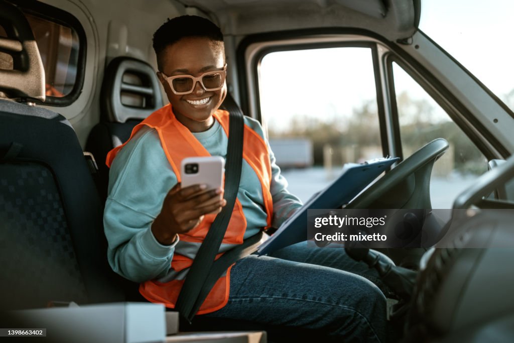 Jovem sorridente motorista de entrega de mulheres mensagens de texto enquanto trabalha