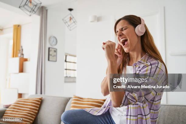 young woman in casual clothes singing using her mobile phone as a microphone while listening to music with wireless headphones. concept of free time at home. - singing fotografías e imágenes de stock