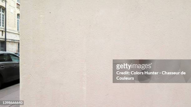 empty wall painted and weathered in beige with a blurred background of a partial view of a car parked on the street and the facade of a building in paris - car front view no people stock-fotos und bilder