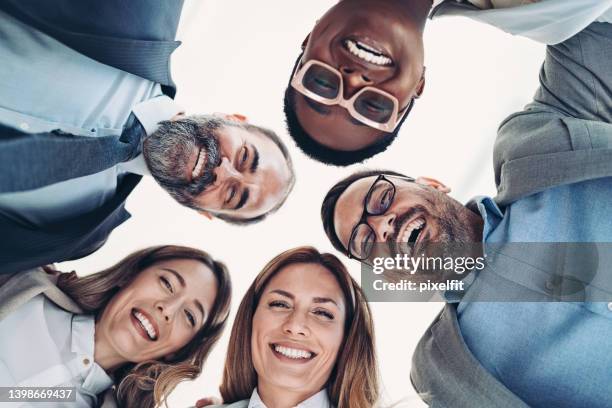 smiling business team bending over in a circle - group of businesspeople standing low angle view stock pictures, royalty-free photos & images
