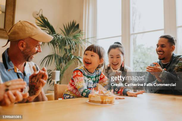 a delighted young girl enjoys the attention of adults who clap for her as she blows out her birthday candles - chinese birthday stock-fotos und bilder