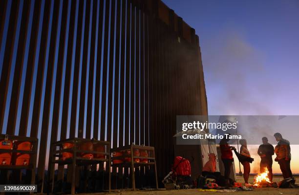 Immigrants from Cuba and Venezuela warm themselves by a fire before sunrise along the U.S.-Mexico border barrier as they await processing by the U.S....