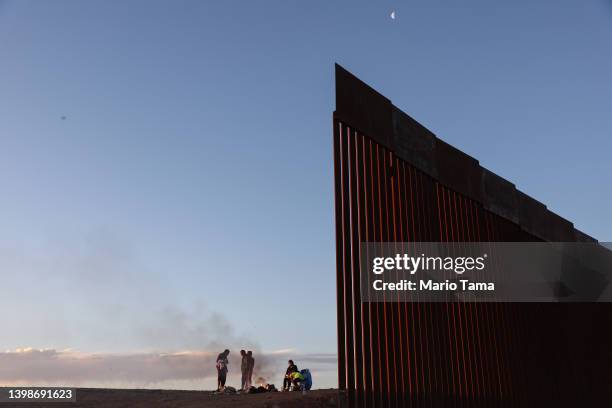 Immigrants from Ecuador warm themselves by a fire beneath the moon along a gap in the U.S.-Mexico border barrier, as they await processing by the...