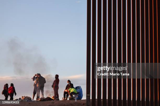 Immigrants from Ecuador warm themselves by a fire after sunrise along a gap in the U.S.-Mexico border barrier, as they await processing by the U.S....