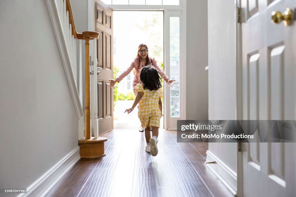 Toddler girl running to greet mother in doorway as she gets home from work