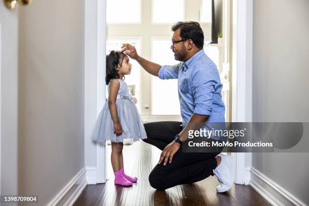 father measuring toddlers daughter's height against wall at home - asia child glasses stock-fotos und bilder