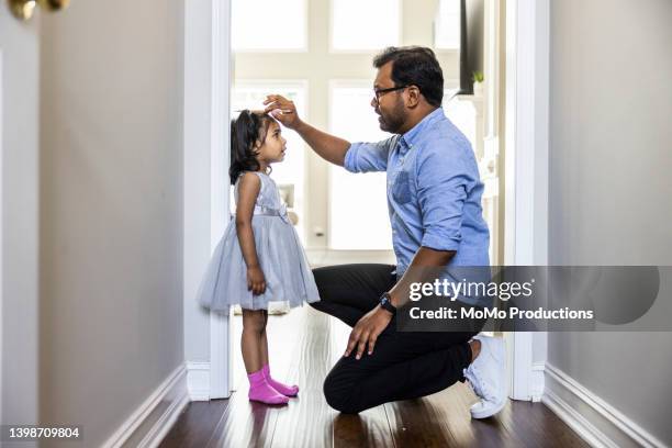 father measuring toddlers daughter's height against wall at home - kids growth chart stock pictures, royalty-free photos & images