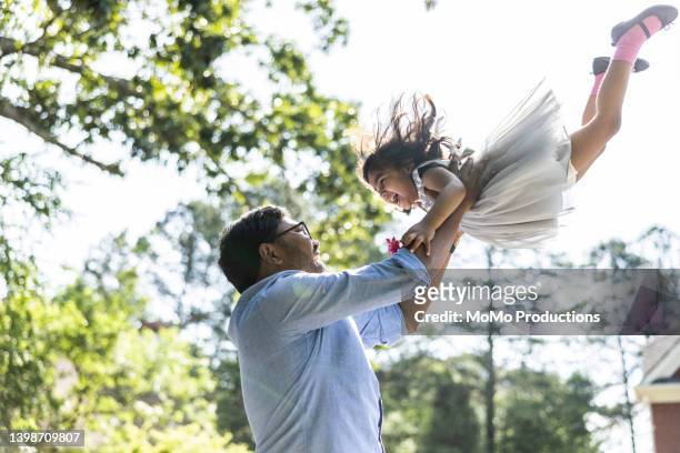 father lifting toddler daughter in the air in front of suburban home - dad throwing kid in air stockfoto's en -beelden