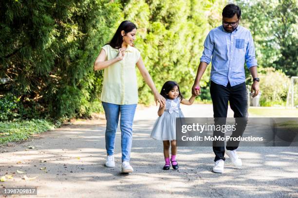 family walking  with toddler daughter on suburban street - dreiviertel vorderansicht stock-fotos und bilder